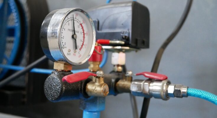 A close-up of a mechanical gauge on a compressed air system with blue pipes, blue tubes, and brass and silver fittings.