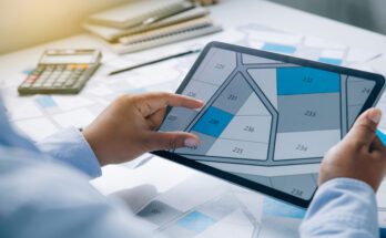 A man's point of view as he examines a map of land parcels on an electronic tablet, with some lots shaded in blue and grey.