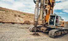 A large industrial rotary drilling machine sits outside, making holes in the dirt at an empty worksite.
