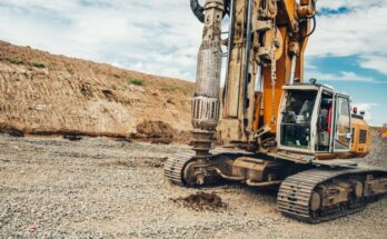 A large industrial rotary drilling machine sits outside, making holes in the dirt at an empty worksite.