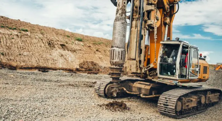 A large industrial rotary drilling machine sits outside, making holes in the dirt at an empty worksite.