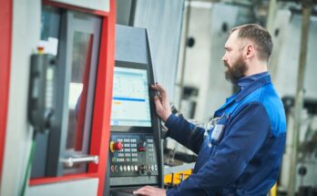 A CNC machine operator in a blue jumpsuit inspects a screen of data analytics attached to his CNC machine.