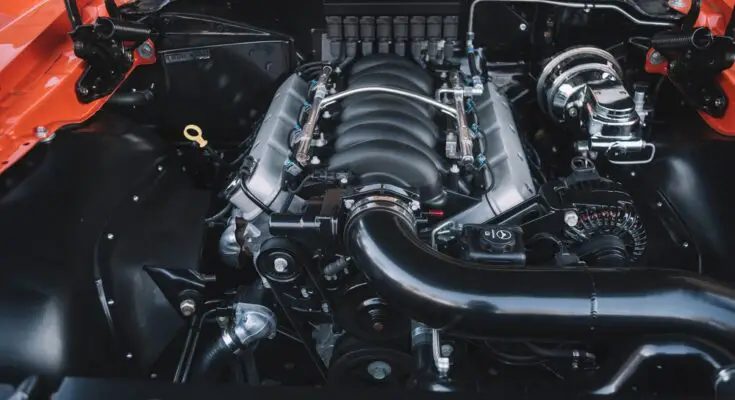 A close-up of an orange vehicle's open hood reveals a large engine with an intricate system of parts.