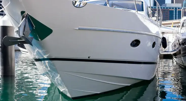 A close-up of the hull of a large white and black boat docked at a marina with tall buildings in the background.