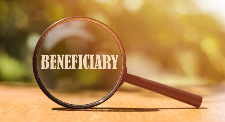 A brown handheld magnifying glass sits on a wooden surface, magnifying the cream-colored word "beneficiary."