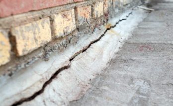An extreme close-up shot reveals a crack extending through a brick foundation and the adjacent pavement.