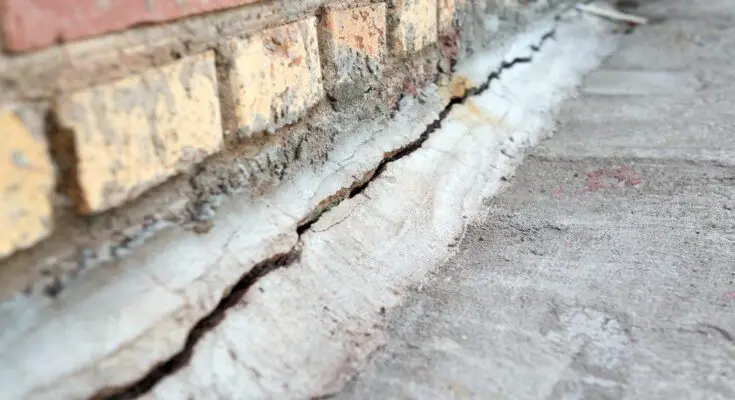 An extreme close-up shot reveals a crack extending through a brick foundation and the adjacent pavement.