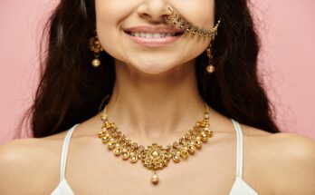 A young woman with elaborate gold earrings, a gold necklace, and a gold nose ring with a chain connecting to her left ear.