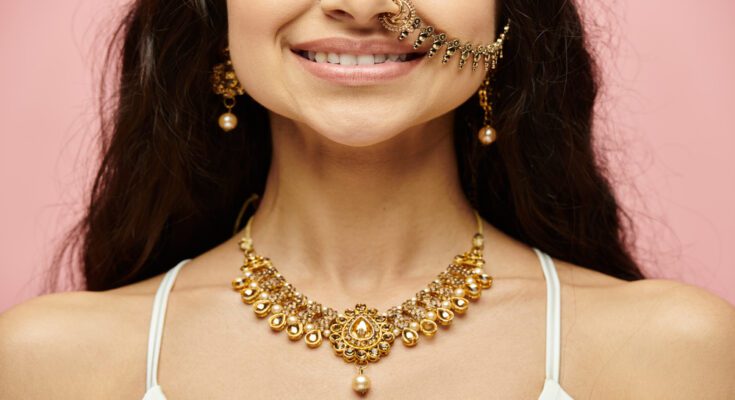 A young woman with elaborate gold earrings, a gold necklace, and a gold nose ring with a chain connecting to her left ear.