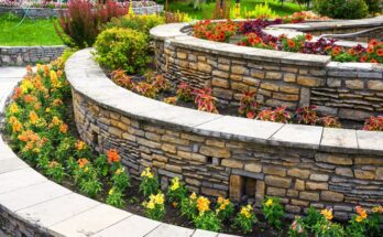 A retaining wall in a home's backyard has multiple levels and different colorful flowers and plants on each tier.