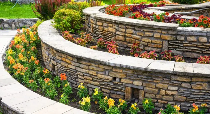 A retaining wall in a home's backyard has multiple levels and different colorful flowers and plants on each tier.