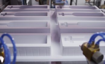 White plastic molds with custom cutouts designed to protect products during shipping, shown in a manufacturing facility.