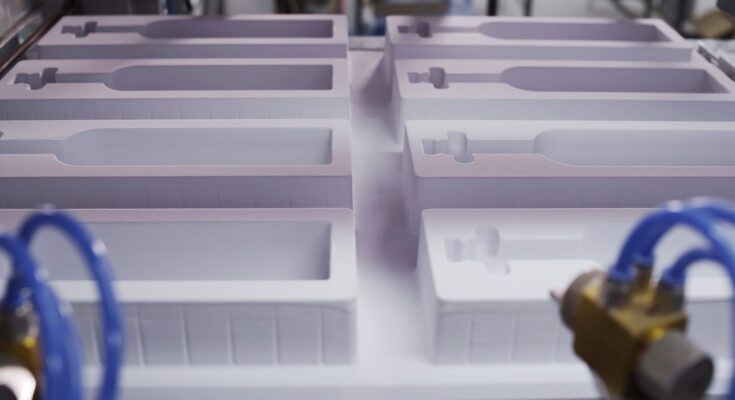 White plastic molds with custom cutouts designed to protect products during shipping, shown in a manufacturing facility.