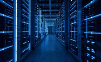 A long hallway in a data center is lined with storage enclosures full of computers, each giving off a blue hue.