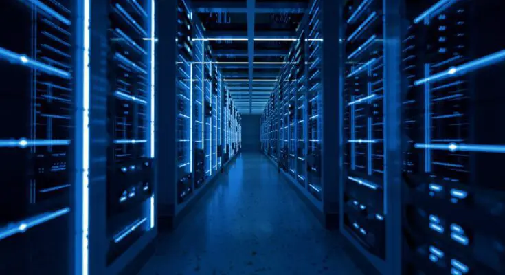 A long hallway in a data center is lined with storage enclosures full of computers, each giving off a blue hue.