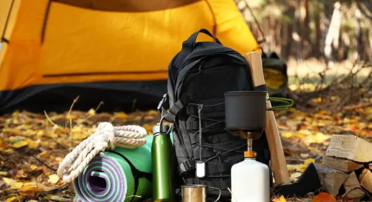 A pile of camping supplies sitting outside the tent. There is a backpack, a water bottle, and a mat.