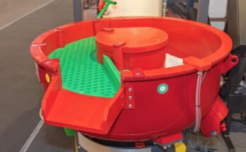 A red vibratory finishing machine in an industrial facility. The machine has a green tray inside it.