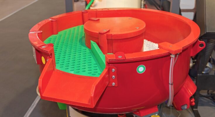 A red vibratory finishing machine in an industrial facility. The machine has a green tray inside it.