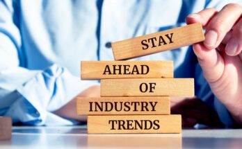 Close-up of a person's hands as they stack up a series of wooden blocks that read "Stay Ahead of Industry Trends."