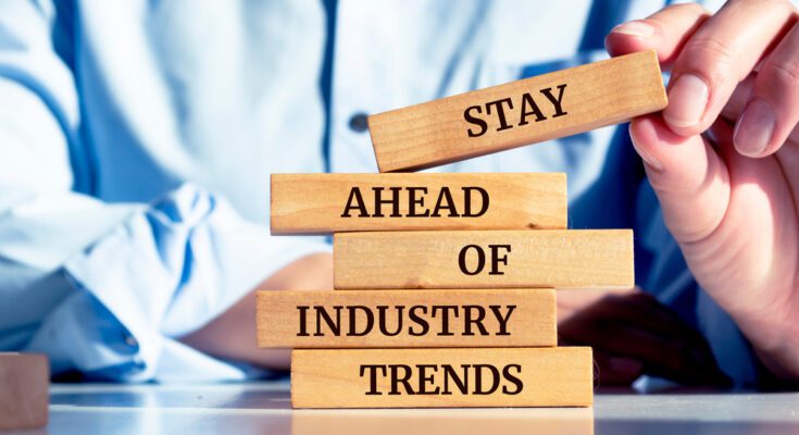 Close-up of a person's hands as they stack up a series of wooden blocks that read "Stay Ahead of Industry Trends."