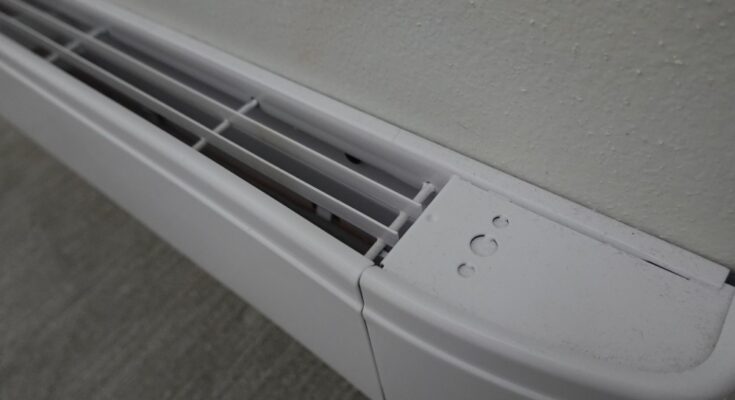 A white baseboard heater along a white wall. The heater has a top vent fully open, with three small indents on the end.