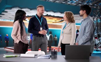 A group of four business professionals huddled around a table at a trade show with various materials laid out.