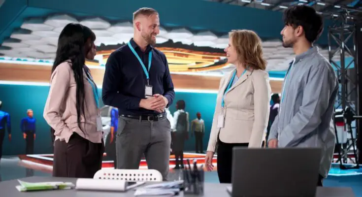 A group of four business professionals huddled around a table at a trade show with various materials laid out.