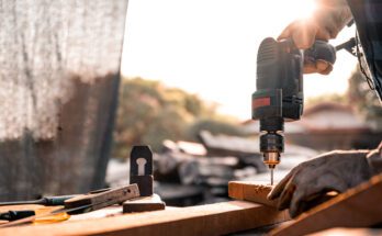 A close-up of a carpenter using a drill while working at home on a wooden floor for home improvement.