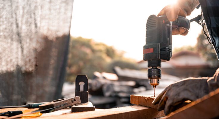 A close-up of a carpenter using a drill while working at home on a wooden floor for home improvement.