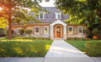 A traditionally styled home with a walkway that goes across the lawn. The front door is framed by two pillars.