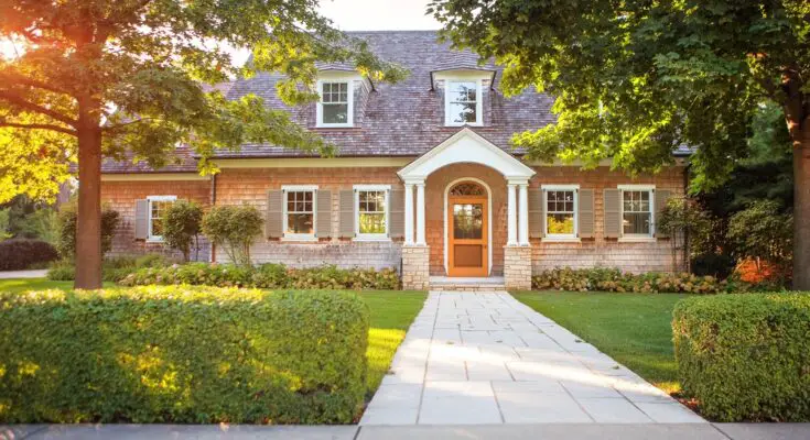 A traditionally styled home with a walkway that goes across the lawn. The front door is framed by two pillars.