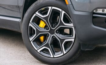 The wheel of a modern car turned slightly inward towards the vehicle. The metal is shiny with black accents.