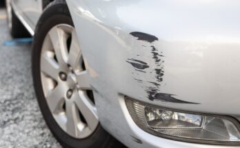A front car bumper with minor damage on it. The silver paint is scraped off, revealing a dark grey underlayer.