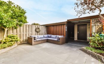 A home's backyard with white weather-resistant sofas, a wreath, and wooden fences, surrounded by greenery.