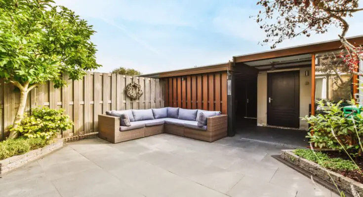 A home's backyard with white weather-resistant sofas, a wreath, and wooden fences, surrounded by greenery.