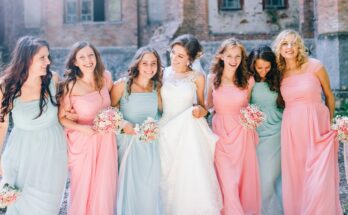 A bride in a wedding gown standing beside six women wearing long pink or blue dresses, each holding a bouquet of flowers.