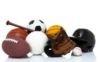 A football, basketball, baseball, soccer ball, volleyball, black baseball helmet, and a baseball glove sit in a pile.