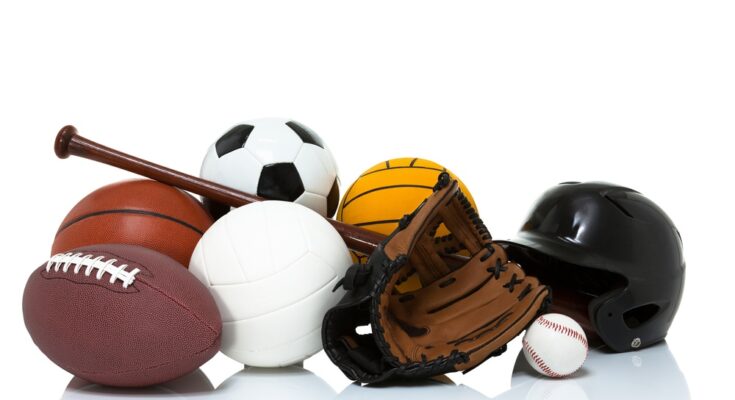 A football, basketball, baseball, soccer ball, volleyball, black baseball helmet, and a baseball glove sit in a pile.