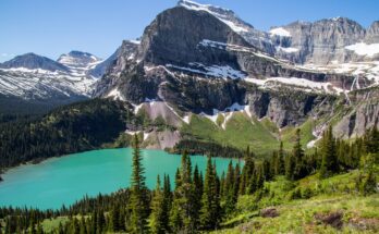 A beautiful view of Glacier National Park. A small lake sits in front of a mountainside covered in snow.