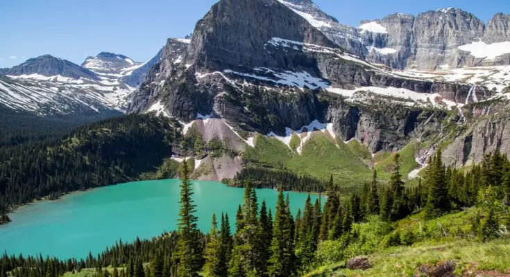 A beautiful view of Glacier National Park. A small lake sits in front of a mountainside covered in snow.