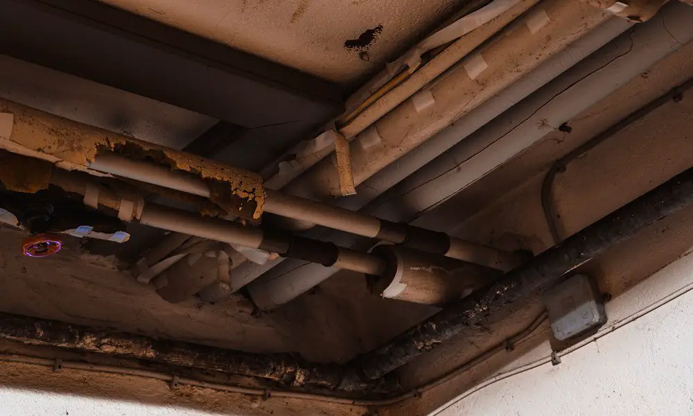 Old plumbing pipes located in the ceiling of a home. Some parts of the system look like they're falling apart.