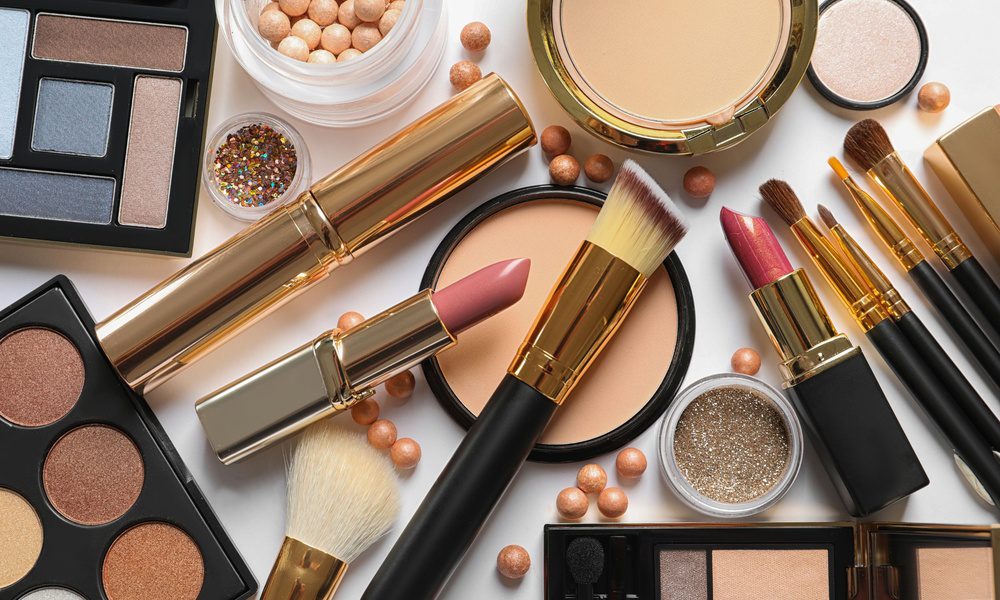 A counter contains a set of makeup products including lipsticks, brushes, palettes, powders, and glitter.