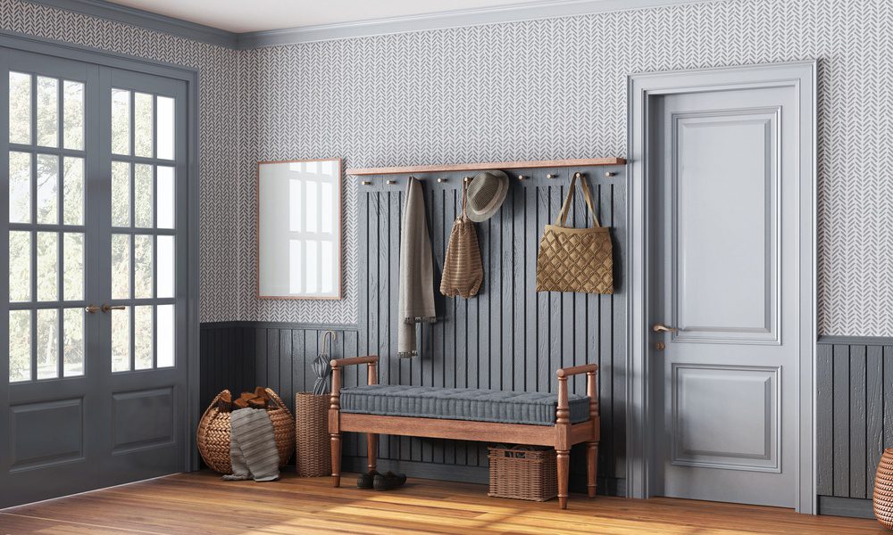 An entryway to a residential home. There is a bench and a coat rack on the wall. There is a purse hanging from the coat rack.