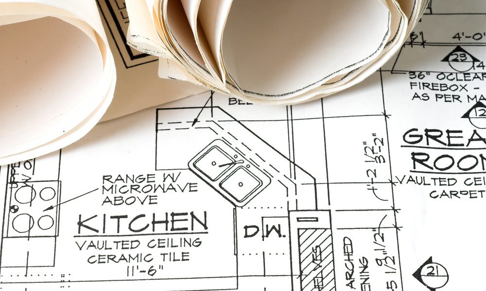 Blueprints for a kitchen remodel sitting open on a flat surface. Two more blueprints are rolled up on the document.