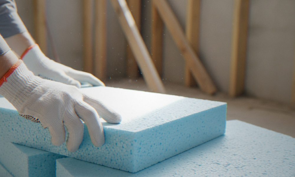 A worker wearing protective gloves is handling rigid foam insulation boards during a construction or renovation project.