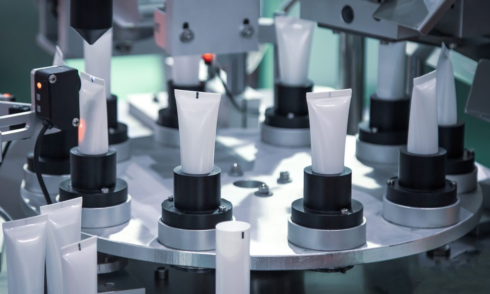 An automatic machine filling rows of plastic tubes on a clean industrial production line with metal equipment.