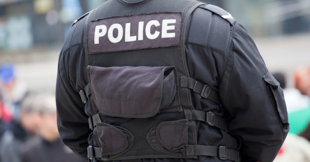 A uniformed police officer with blue fabric and dark duty gear visible at the waist, shown from close range.