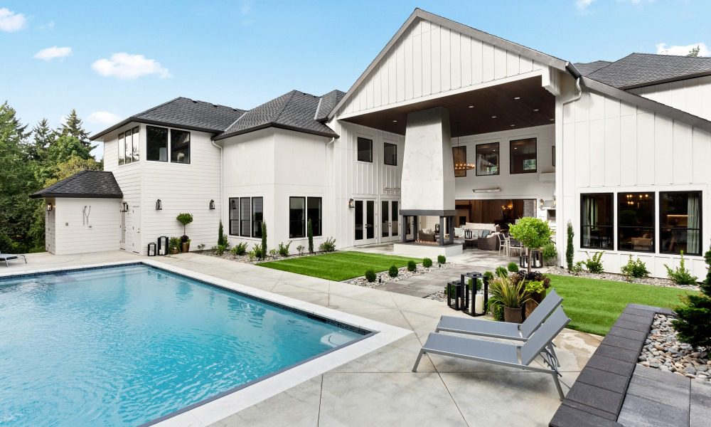 A backyard space with an in-ground swimming pool, lounge seats, and a covered seating area with a fireplace.