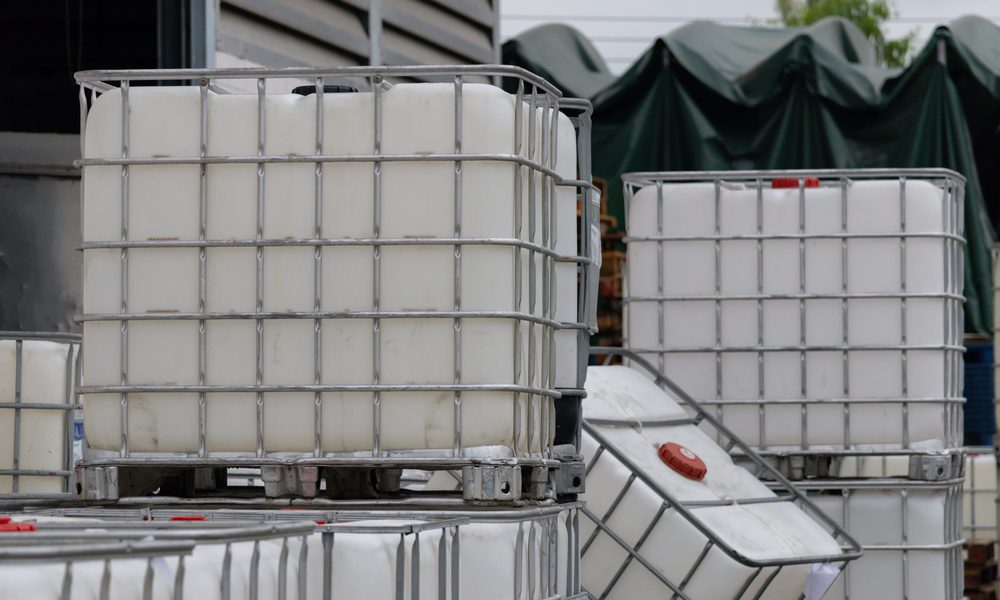 Several IBCs clustered in a yard with some stacked on top of another. Metal cages surround each container.