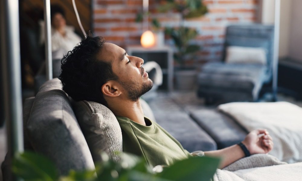 A man relaxes on a chair with an IV drip, resting quietly in a bright clinic during a wellness infusion.